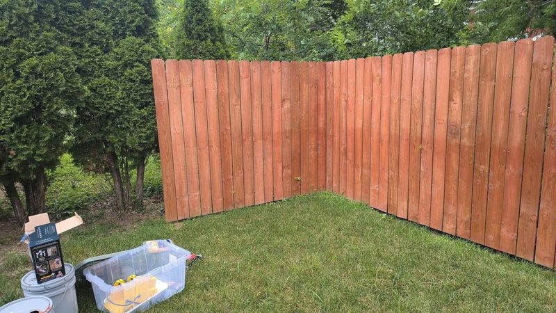 Weathered cedar fence corner with faded reddish stain, before