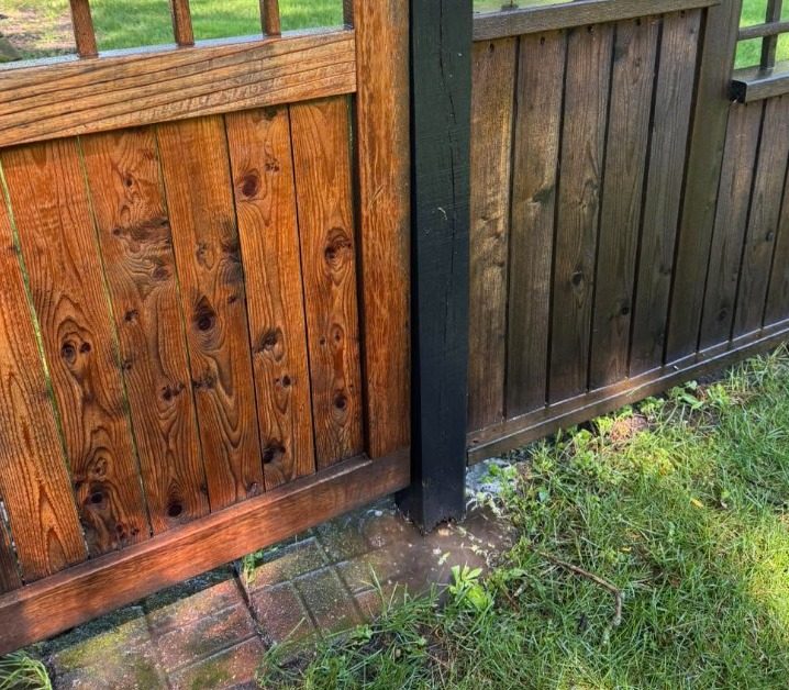 Freshly stained wood gate and fence panel with a dark post between them