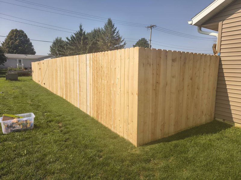 Bare new cedar dog-ear privacy fence around a backyard, before stain