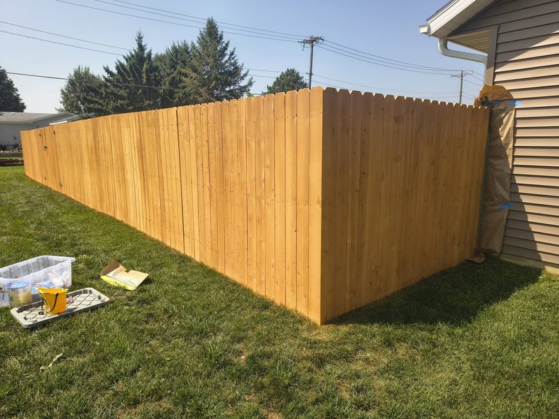 The same cedar privacy fence after a warm semi-transparent stain, siding masked with paper